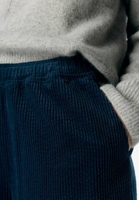 Pantalons en velours côtelé bleu marine à rayures verticales, avec une taille élastique et des poches latérales, associés à un pull en tricot gris clair.