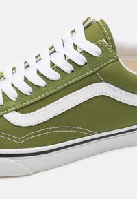 Zielone płócienne sneakersy z białymi sznurowadłami i akcentami po bokach, z białą gumową podeszwą i detalami w czarnym kolorze. Teksturowana powierzchnia z przeszyciami.