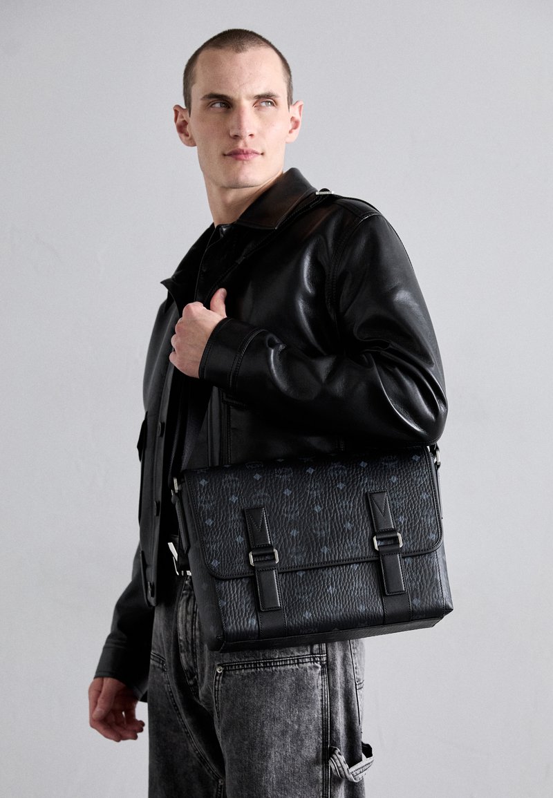 Borsa a tracolla in pelle nera con superficie testurizzata, dotata di un bavaglino, due fibbie in metallo e sottili dettagli a motivo.