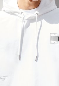 Felpa bianca con cappuccio e hardware in argento per il cordoncino, caratterizzata da una toppa con logo. Realizzata in tessuto morbido, evidenzia un design minimalista.
