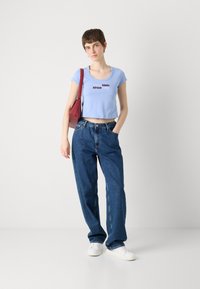 Light blue cropped t-shirt with white and red "Calvin Klein since 1968" text, paired with loose-fitting dark blue jeans and white sneakers.