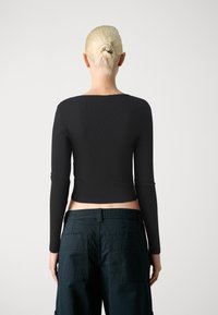 Svart langermet topp med en tettsittende design, ribbet tekstur og rett nederkant, sammen med mørkegrønne cargobukser med baklommer.