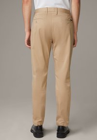 Beige Chinos mit geradem Schnitt, aus einem glatten Stoff gefertigt. Mit geknöpften Gesäßtaschen und einem normalen Bund.