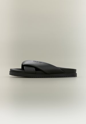 Sandalia de slide negra con correas anchas cruzadas y suela texturizada sobre fondo neutro.