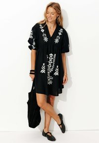 Robe noire avec broderie florale blanche, manches bouffantes courtes, décolleté en V, coupe décontractée, assortie à un sac noir et des chaussures à motifs.