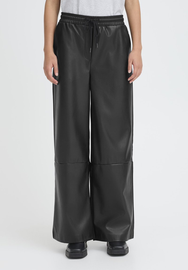 Pantaloni a gamba larga in similpelle nera con vita elasticizzata e coulisse. Texture liscia, con dettaglio a cucitura al ginocchio.