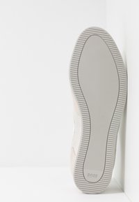 Béžové semišové tenisky s gumovou podrážkou, s texturovaným povrchem a kontrastním bílým prošíváním. Diskrétní značení na boku.