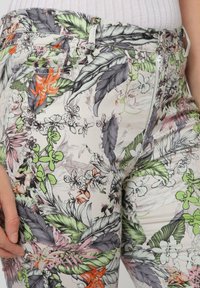 Pantalones de tela ligera con estampado floral que presentan hojas verdes, flores naranjas y detalles intrincados. Incluyen cierre de cremallera y bolsillos frontales.