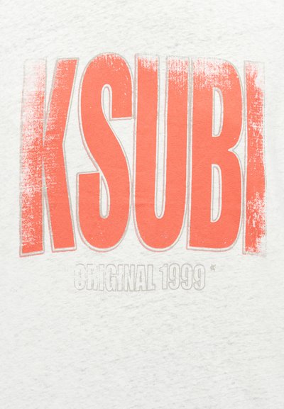 Λευκό βαμβακερό μπλουζάκι με τον έντονο, φθαρμένο πορτοκαλί λογότυπο "KSUBI" και μικρότερο γκρι κείμενο που αναγράφει "ORIGINAL 1999" κάτω από αυτό. Απλός σχεδιασμός, κοντά μανίκια.
