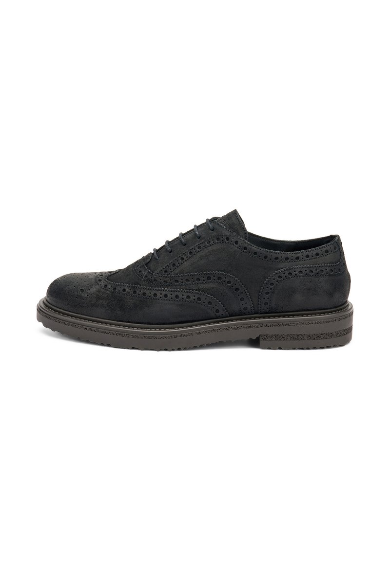 Scarpa brogue in suede nero con perforazioni dettagliate e una spessa suola in gomma, vista di lato.