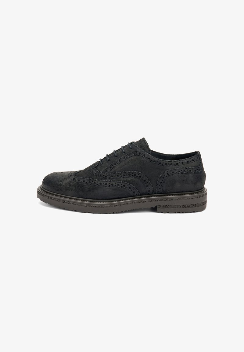 Scarpa brogue in suede nero con perforazioni dettagliate e una spessa suola in gomma, vista di lato.