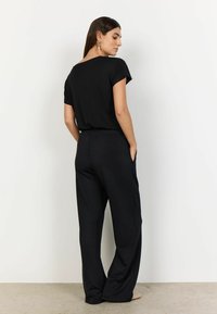 Black short-sleeve top with a wide neckline paired with loose black pants. Smooth fabric texture and side pockets on the pants.