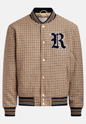 Ruskea houndstooth-kuvioinen bomber-takki, jossa on tummansininen ribba kauluksessa ja hihoissa. Takissa on valkoinen brodeerattu 'R' ja kultaiset napit.