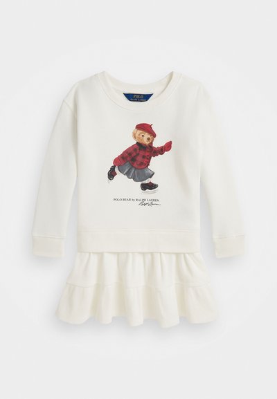 Balta garo piedurkņu kleita ar viļņotu apakšmalu, kurā attēlots polo lācis sarkanas rūtainas krekliņas un beretes apģērbā. Mīksta tekstūra, ikdienišķs dizains.