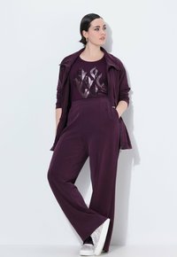 Paarse matching set bestaande uit een lange mouwen zipjack en wijde broek. De top heeft een metallic patroon; de schoenen zijn glinsterend en wit.
