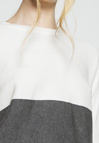 Maglione leggero in bianco e grigio scuro con blocchi di colore orizzontali, texture a coste e vestibilità comoda.
