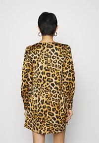 Leopard print dress featuring a shiny fabric with a relaxed silhouette, long sleeves, and a back slit detail. Colors include gold, black, and brown.