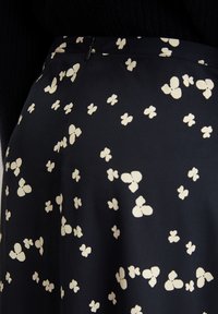 Schwarzer Stoffrock mit einem Muster aus kleinen, cremefarbenen Schmetterlingen. Mit einem seitlichen Reißverschluss zum Verschließen. Weiche Textur.