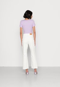 Top justo em roxo claro com mangas escallopadas, combinado com calças brancas de perna larga de cintura alta e sapatos de salto bloco em roxo claro.