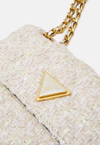 Gėlėtas kreminės spalvos maišelis, pagamintas iš tekstūruotos medžiagos, su auksinės grandinės dirželiu ir trikampiu auksiniu logotipo akcentu priekyje.