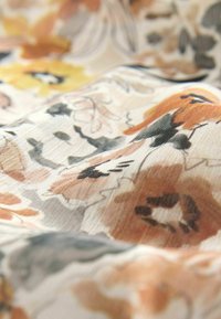Tissu doux avec un motif floral comprenant de grandes fleurs abstraites dans des tons orange, jaune, beige et gris foncé atténués.