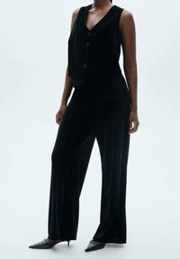 Černý sametový overal s bezramínkovým, na knoflíky zapínaným vrškem a nohavicemi s širokým střihem, který se pyšní jemnou texturou a přizpůsobeným střihem.