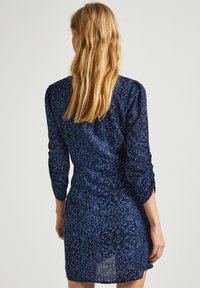 Námornícky modré šaty s vzorom, dlhými naberanými rukávmi a priliehavým strihom, zdobené zložitými svetlomodrými kvetinovými motívmi.