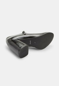 Black patent leather high-heeled shoe with a square heel and smooth texture. Features a subtle buckle detail and non-slip sole.