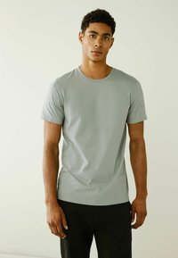 Lichtgrijze ronde hals t-shirt van zachte stof, met korte mouwen en een aansluitende pasvorm. Gecombineerd met donkere broeken.