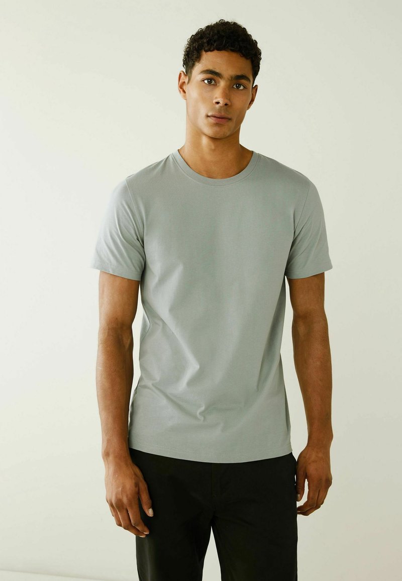 Lichtgrijze ronde hals t-shirt van zachte stof, met korte mouwen en een aansluitende pasvorm. Gecombineerd met donkere broeken.