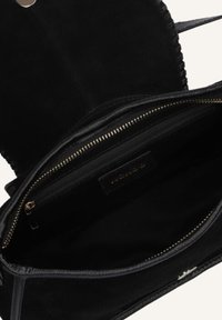 Zwarte suède handtas met een textuurafwerking, voorzien van een ritsvak en gouden hardware accenten, met een ruime binnenkant.