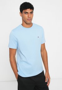 Ανοιχτό μπλε βαμβακερό μπλουζάκι με κλασική στρογγυλή λαιμόκοψη, κοντά μανίκια και μικρό λογότυπο στην αριστερή πλευρά του στήθους. Λείος υφασμάτινος τύπος.