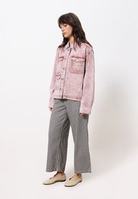 Helle rosa Jeansjacke mit zwei vorderen Taschen, kombiniert mit weiten schwarz-weißen gestreiften Hosen und beigen flachen Schuhen.