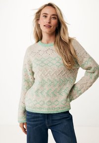 Stickad tröja i beige med gröna geometriska mönster. Har rund hals, långa ärmar och strukturdetaljer överallt. Mjuk, chunky tyg.