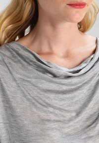 Top grigio, morbido, con scollo ampio, caratterizzato da un tessuto liscio e una leggera lucentezza, indossato su spalle scoperte.