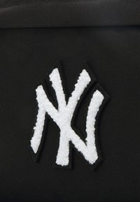 Nahaufnahme eines schwarzen Stoffruksacks mit einem weißen, gestickten NY-Logo, das über Texturdetails und einen schwarzen Rand um das Logo verfügt.