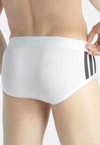 Slip bianchi in cotone con una texture liscia, dotati di una cintura flessibile e tre strisce nere sui lati.