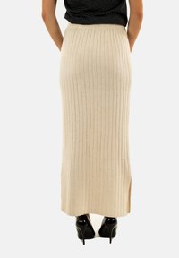 Gonna maximale beige a maglia con texture a coste verticali, spacco laterale e vita elastica. Abbinata a scarpe con tacco alto nere.