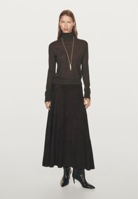 Brown turtleneck sweater paired with a long, dark, textured skirt. Black heeled ankle boots and a silver pendant necklace complete the outfit.