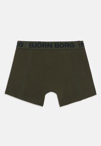 Grønne boksershorts laget av myk bomull, med et marineblått midjebånd som har teksten "BJÖRN BORG" og flate sømmer.