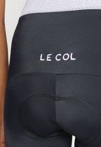 Fekete kerékpáros rövidnadrág párnázott ülőrésszel, sima textúrával és hímzett "LE COL" logóval a hátsó részen.