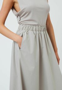 Jupe avec taille élastique gris clair, texture froncée et poches sur les côtés. Tissu lisse avec une coupe décontractée et un design minimaliste.