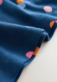 Tessuto blu con cuciture visibili e pois colorati in rosa, arancione e viola, leggermente piegato su una superficie chiara.