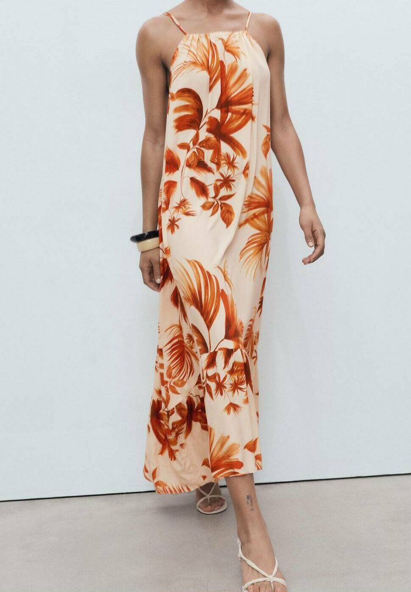 Robe maxi en pêche clair avec des motifs floraux rouges, bretelles spaghetti et un ourlet évasé. Caractérisée par un tissu lisse et léger.