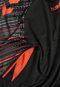 Jersey deportivo negro con un patrón texturizado en negro y gris, resaltado por acentos naranjas y detalles de malla en el dobladillo.