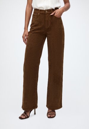 Femme portant un pantalon en velours côtelé marron taille haute à jambes larges avec poches avant et des sandales marron à talons hauts et brides.