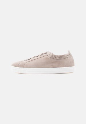 Lys beige semsket lavt sneakers med hvit såle, elastisk ankelåpning og metallhemper til snøring, vist fra siden på hvit bakgrunn.
