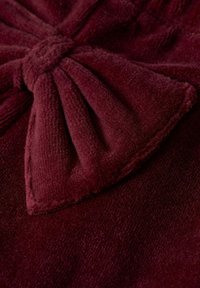 Bordeaux stof met een zachte, gestructureerde afwerking. Heeft een geknoopt strikdetail, dat een verhoogd ontwerpelement op het materiaal creëert.