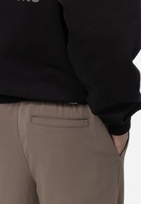 Svart sweatshirt med ribbat manschett, i kombination med taupe-byxor som har en bakficka och en slät, vävd struktur.