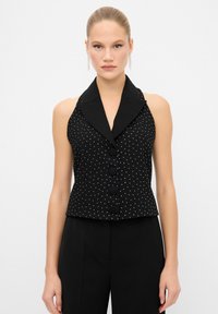 Schwarzes Tanktop mit einem eingeschnittenen Kragen, gepunktetem Muster und fünf Knöpfen vorne. Glatte Textur mit einer taillierten Passform.